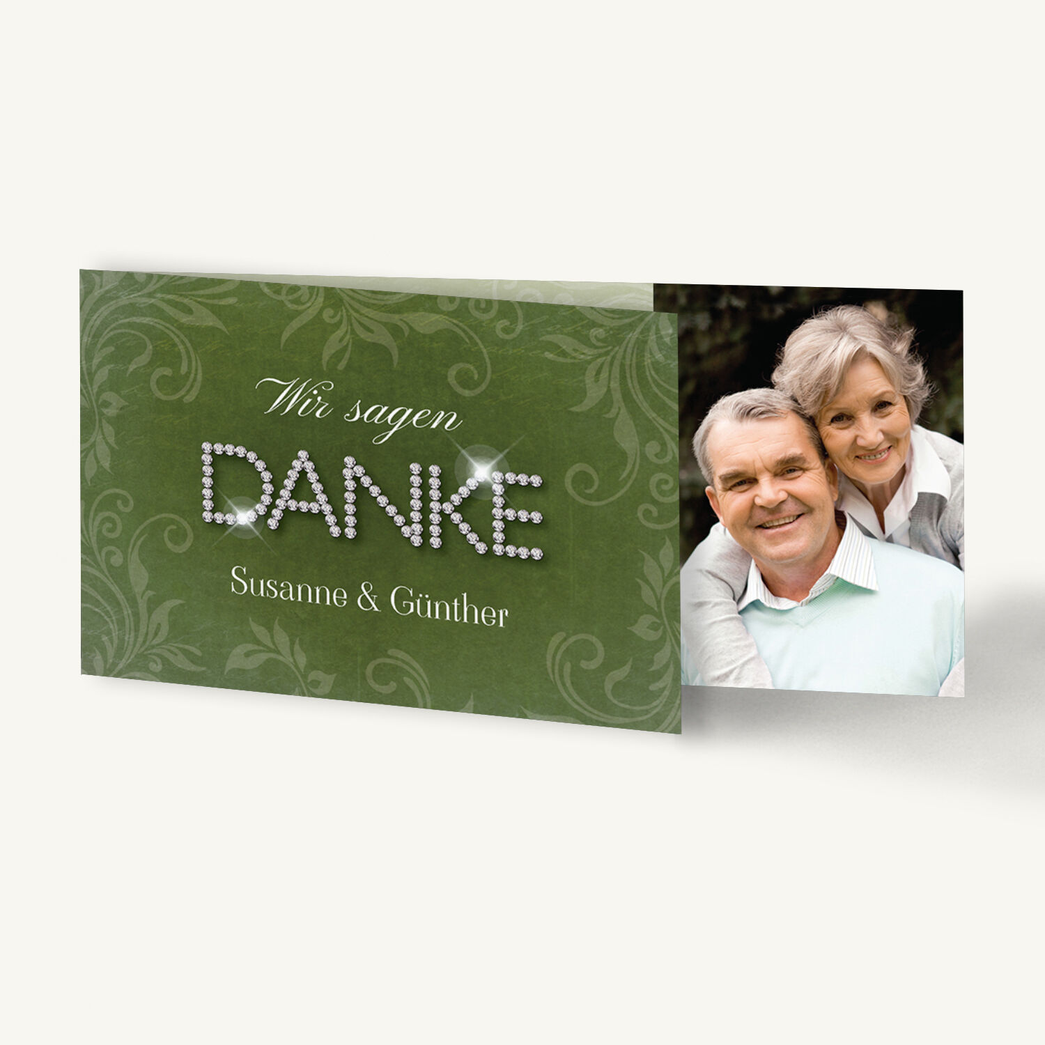 Elegante Danksagungskarte zur Diamantenen Hochzeit im Querformat 21 × 10 cm. Die Vorderseite zeigt einen edlen, grün strukturierten Hintergrund mit floralem Ornamentmuster. Darauf steht in schwungvoller, weißer Schrift ‚Wir sagen‘ und darunter das Wort ‚DANKE‘, das aus funkelnden, silbernen Schmucksteinen gebildet ist. Unterhalb sind die Namen ‚Susanne & Günther‘ in feiner Serifenschrift zu lesen. Im aufgeklappten Innenteil ist ein Foto eines älteren, lächelnden Paares zu sehen – ein harmonisches, liebevolles Motiv, das Dankbarkeit und Lebensfreude ausdrückt.