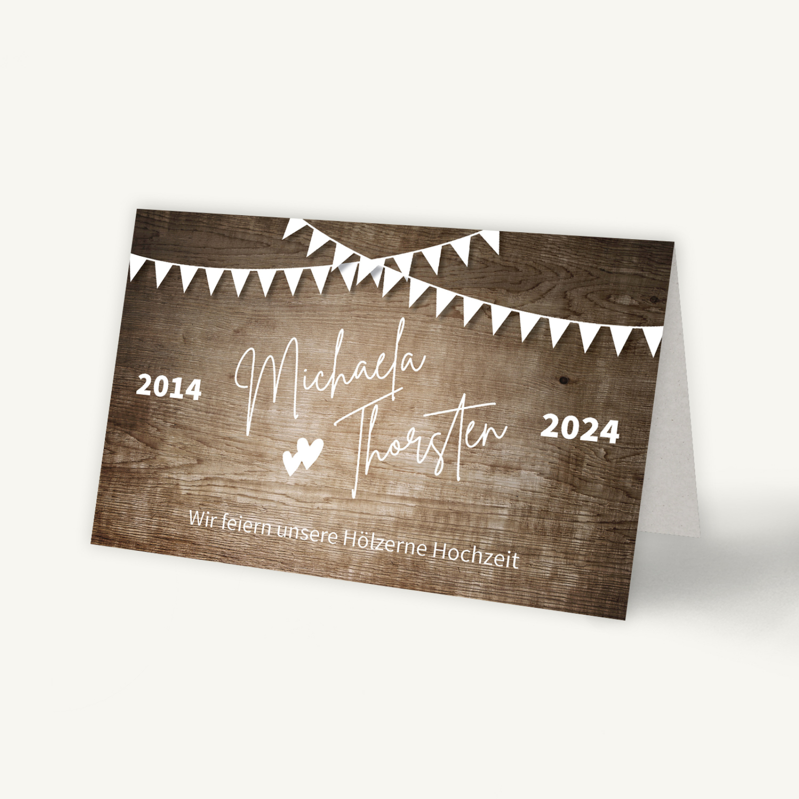 Einladungskarte zur Hölzernen Hochzeit mit rustikalem Holz-Hintergrund. Oben hängen weiße Wimpelgirlanden. In der Mitte stehen die Namen 'Michaela & Thorsten' in eleganter Schrift, dazwischen zwei kleine Herzen. Links und rechts die Jahreszahlen '2014' und '2024', darunter der Text 'Wir feiern unsere Hölzerne Hochzeit'. Ein schlichtes, natürliches Design mit festlicher Note.
